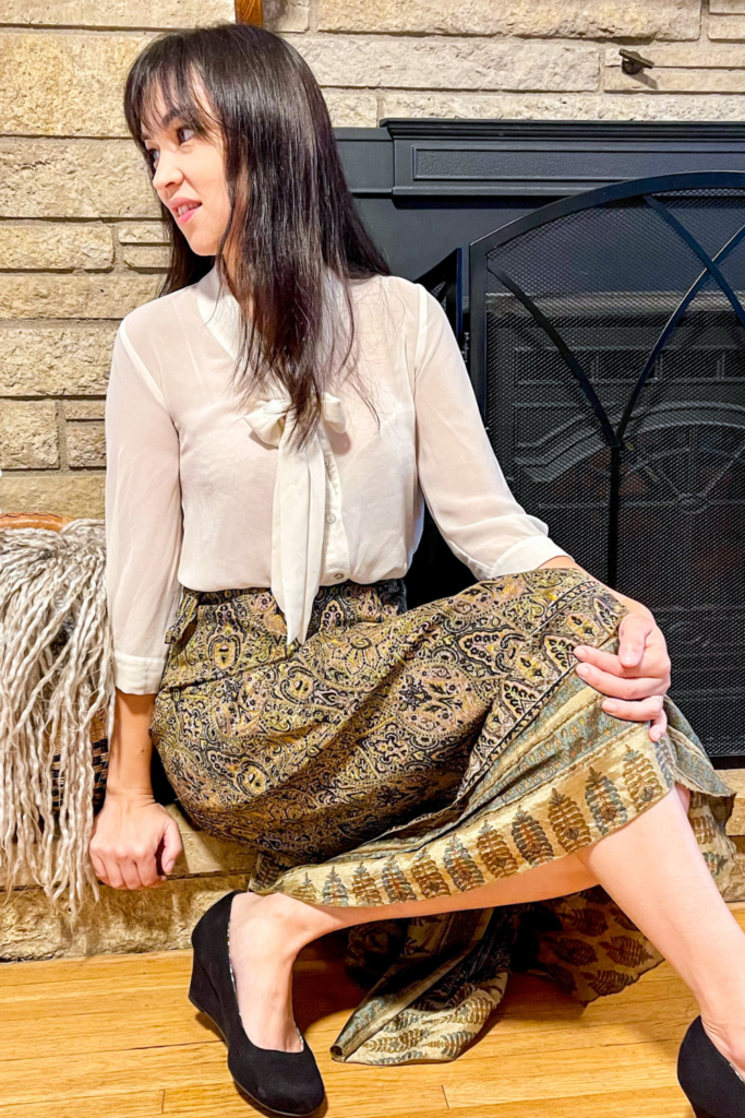 a person sitting on the floor in front of a fireplace wearing a white button up top and brown skirt