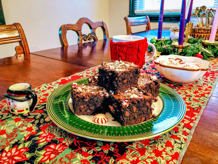 Brownies on a green gold and white plate, with a snow man cup off to the side.
