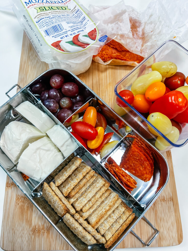 Pizza Snacker lunch includes tomatoes, pepperoni, shredded wheat crackers, fresh mozzarella cheese, and grapes in the 5-compartment ecozoi lunch tin.
