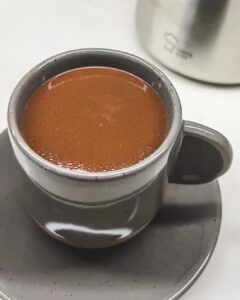 a cup of hot chocolate sits on a saucer next to a metal carafe